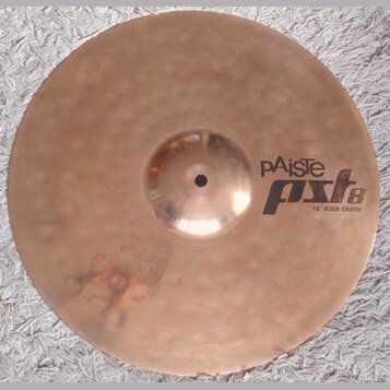 Kruhový mosazný činel s viditelným kovánívým povrchem. Na pravé straně je černý nápis pAiste a pod ním model PST 8 s doplňkem 16" ROCK CRASH. Povrch…