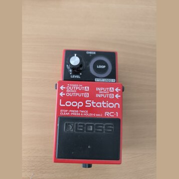 Červený efekt pedál s černým spínacím pedalem a ovládacími prvky. Na zařízení jsou nápisy CHECK, LOOP, LEVEL, STOP/UNDO, OUTPUT A (MONO), INPUT A (MO…