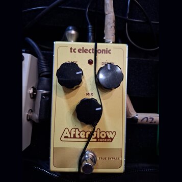 Žlutý efekt pedál s nápisy tc electronic, Afterglow a CHORUS. Na horní části jsou dva černé oválné knoflíky s popisky RATE a DEPTH, uprostřed je jede…