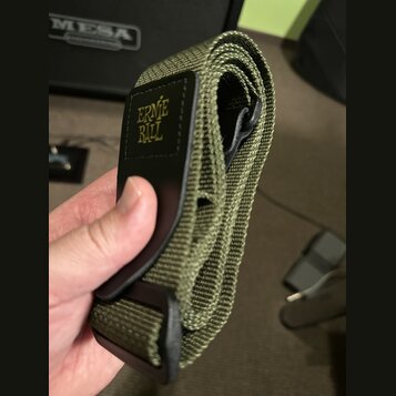 Zvolněný kytarový popruh v olivově zelené barvě z textního materiálu. Na černé kožené části je žlutý nápis ERNIE BALL. Popruh vykazuje mírné známky p…