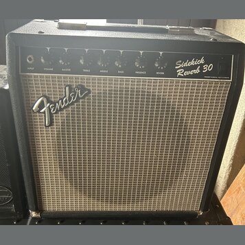 Kytarový kombo zesilovač v černém obalu s hnědou textilní maskou. Na horním ovládacím panelu jsou nápisy Sidekick Reverb 30 a Fender Musical Instrume…