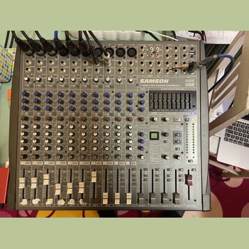 Šedý mixovací pult s nápisy SAMSON L1200 LIVE MIXING CONSOLE, 24 DSP a USB. Zařízení obsahuje řadu vstupních kanálů s potenciometry, přepínači a posu…