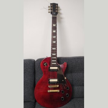 Červená elektrická kytara s dumpedým topem a černým pickguardem. Na hlavě hmatníku je nápis Epiphone. Kytara má dva humbuckery se zlatými kryty, čtyř…