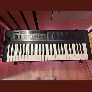 Černý syntetizátor s klávesnicí a ovládacím panelem. Na horní části je bílý nápis KORG POLY 800 MK II a červené digitální displeje. Panel obsahuje řa…