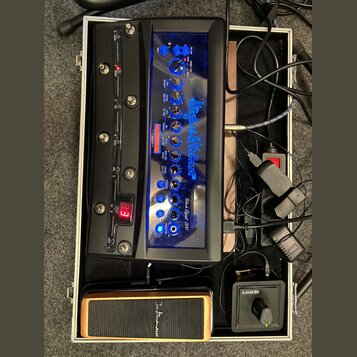 V hliníkovém kufru se nachází černý kytarový procesor s modře podsvíceným panelem a nápisem Hughes & Kettner Black Spirit 200. Zařízení obsahuje řadu…