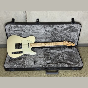 Elektrická kytara typu Telecaster v krémové barvě s bílým pickguardem, uložená v černém tvrdém kufru s šedou polstrováním. Na hlavě hmatníku je vidit…
