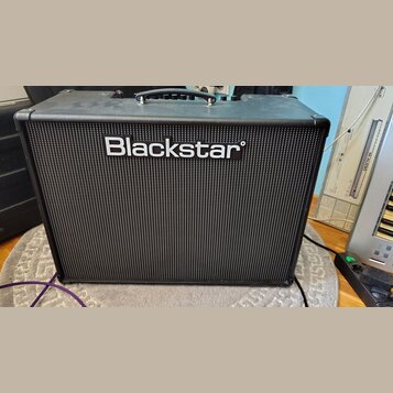 Černý kytarový kombozesilovač s texturovaným povrchem a černou přední maskou. Uprostřed je umístěno bílé logo Blackstar. Nástroj má v horní části čer…