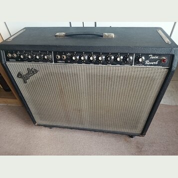 Černý kytarový kombo zesilovač s šedou textilní mřížkou. Na pravé straně je nápis Twin Reverb a na mřížce logo Fender. Horní ovládací panel obsahuje…