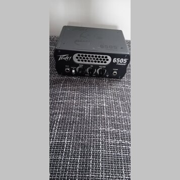 Černý kompaktní kytarový zesilovač s nápisy Peavey a 6505 PIRANHA™. Na předním panelu jsou tři ovládací knoflíky s popisky GAIN, EQ a VOLUME, přepína…