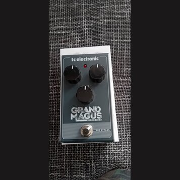 Kytarový efekt pedál v tmavě šedém provedení s bílými nápisy. Na horní hraně je logo tc electronic a uprostřed název modelu GRAND MAGUS DISTORTION. P…