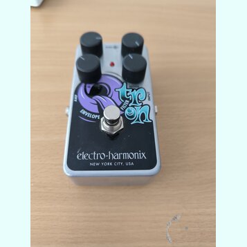 Stříbrný efekt pedál s černým předním panelem a čtyřmi černými ovládacími knoflíky. Na panelu je nápis Electro-Harmonix NEW YORK CITY, USA a grafický…
