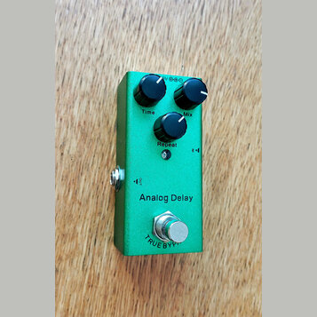 Zelený efekt pedál Analog Delay v kovovém provedení. Na horní straně jsou tři černé oválné ovladače s popisky Time, Mix a Repeat. Ve spodní části je…