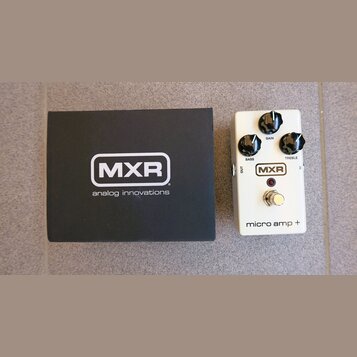 Bílá kytarový efekt pedál s nápisy MXR a micro amp +. Pedál má tři černé ovládací knoflíky s popisky GAIN, BASS a TREBLE, červenou kontrolku a stomeč…