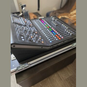 Černý digitální mixážní pult s displejem a množstvím posuvníků, knoflíků a barevných tlačítek. Na pravém předním okraku je bílý nápis MIDAS. Zařízení…