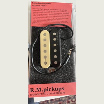 Dva elektrické kytarové snímače typu humbucker v krabičce s polstrováním. Jeden snímač je krémově bílý a druhý černý, oba mají viditelné kovové pólov…