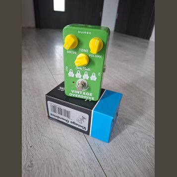 Zelený efekt pedál s nápisem Vintage OVERDRIVE a logem Harley Benton. Má tři žluté oválné ovladače s popisky DRIVE, TONE a VOLUME. Na horní straně je…