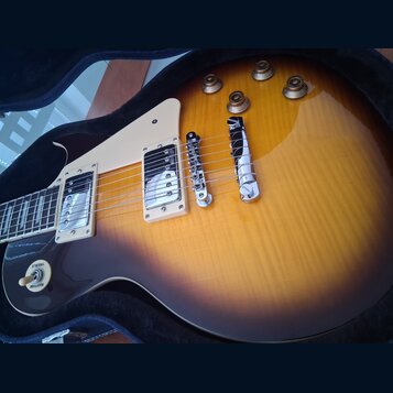 Elektrická kytara typu Les Paul s barevným přechodem od žluté k tmavě hnědé (sunburst). Nástroj má dva humbuckery s krémovými rámečky, chromovaný kob…