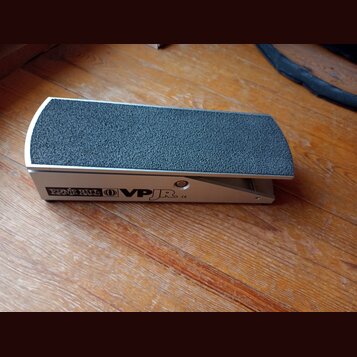 Stříbrný volume pedál s černým, hrubým povrchem šlapáku. Na boku je uveden nápis ERNIE BALL, logo v kruhu a označení VPJR CE. Zařízení vykazuje mírné…