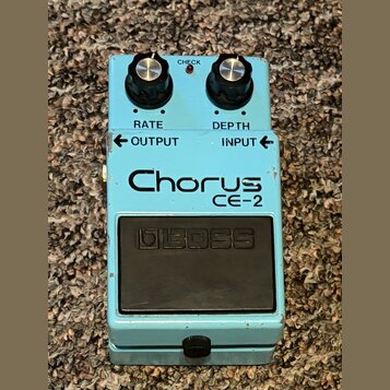 Světle modrý efekt pedál s nápisy RATE, DEPTH, OUTPUT a INPUT. Uprostřed je velký nápis Chorus CE-2 a ve spodní části černý spínací pedál s vyraženým…