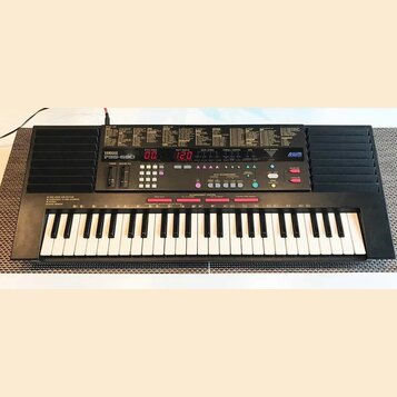 Černý digitální klavír s bílými a černými klávesami. Na ovládacím panelu je nápis YAMAHA PSS-590 a logo AWM. Přístroj obsahuje červené digitální disp…