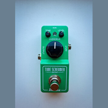 Zelený efekt pedál s nápisy TONE, LEVEL a OVERDRIVE u ovládacích knoflíků. Na spodní části je uveden název modelu TUBE SCREAMER MINI a logo Ibanez. N…