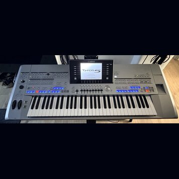 Stříbrný digitální klavír s nápisy YAMAHA a Tyros 5. Nástroj má v horní části displej, na kterém je zobrazen text Tyros 5 a další systémové informace…