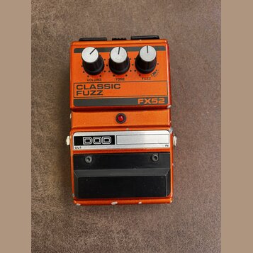 Oranžový efekt pedál s nápisy CLASSIC FUZZ a FX52. Na horní části jsou tři černé ovládací knoflíky s popisky VOLUME, TONE a FUZZ. V dolní části je lo…