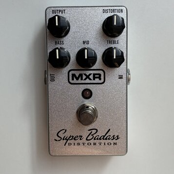 Stříbrný efekt pedál s kovovým, třpytivým povrchem. Na horní části jsou čtyři černé otočné ovladače s nápisy OUTPUT, DISTORTION, BASS, MID a TREBLE.…
