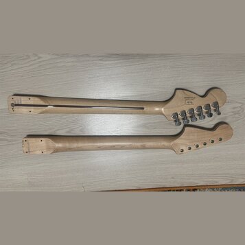 Dvě krky z basové kytary z přírodního světlého dřeva. Horní krk má na hlavě nápis "S/N IC12004069" a logo "Fender". Na hlavě jsou osazeny čtyři kovov…