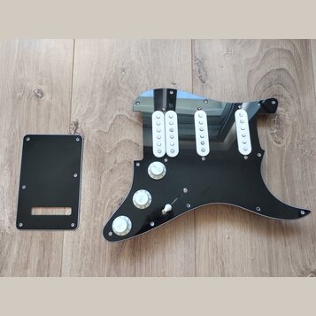 Černý plastový pickguard pro elektrickou kytaru s třemi bílými jednoznačkovými snímači. Na povrchu jsou tři bílé oválné knofíky s nápisy VOLUME, TONE…