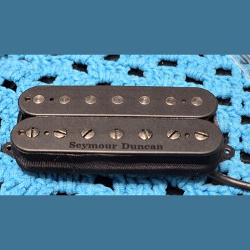 Černý humbucker snímač s plastovým krytem. Na spodní části je bílý nápis Seymour Duncan. Horní cívka má viditelné kovové pólové šrouby, spodní cívka…