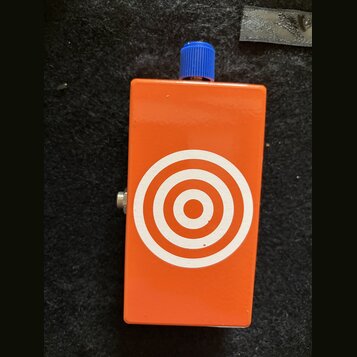 Oranžový efekt pedál s modrým ovládacím knoflíkem. Na přední straně je bílý grafický symbol v podobě soustředných kruhů (terč). Povrch je hladký, bez…