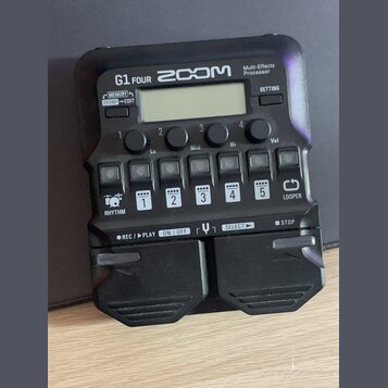 Černý multi-efektový procesor s nápisy G1 FOUR, ZOOM a Multi-Effects Processor. Zařízení obsahuje displej, čtyři ovládací knofíky s popisky Lo, Mid,…