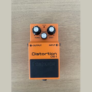 Oranžový efekt pedál s černým stoupacím spínačem. Na zařízení jsou nápisy Distortion DS-1, BOSS, LEVEL, TONE, DIST, CHECK, OUTPUT a INPUT. Povrch ped…