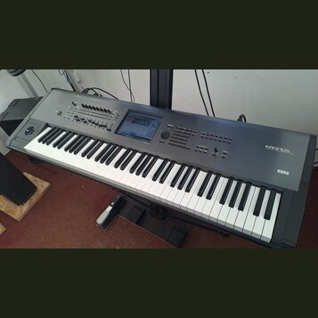 Šedý digitální klavír s černými a bílými klávesami, umístěný na černém stojanu. Na pravé straně jsou bílé nápisy KRONOS MUSIC WORKSTATION a KORG. Nás…