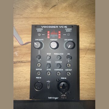 Černý modul s nápisem VOCODER VC16 a logem behringer v dolní části. Zařízení obsahuje několik otočných potenciometrů s popisky CAR SHAPE, FORMANT a E…