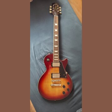 Elektrická kytara s trupem v červeno-žlutém sunburst provedení a hnědým hmatníkem s trapezoidními vložkami. Na hlavě je nápis Gibson, modelové označe…