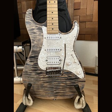 Elektrická kytara typu Stratocaster s tělem z vyvzorovaného dřeva v šedohnědé barvě a hmatníkem ze světlého javoru. Nástroj má bílý pickguard s perle…