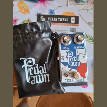 Kytarový efekt s nápisem Pedal lawn a TEXAN TWANG™. Pedál má stříbrné tělo s barevným motivem mapy Texasu v modré a červené barvě, dva ovládací knofl…