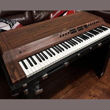Digitální piano v dřevěném korpusu s tmavým povrchem imitujícím masiv. Na horní liště je nápis AHAMAN a několik ovládacích tlačítek s popisky. Kláves…