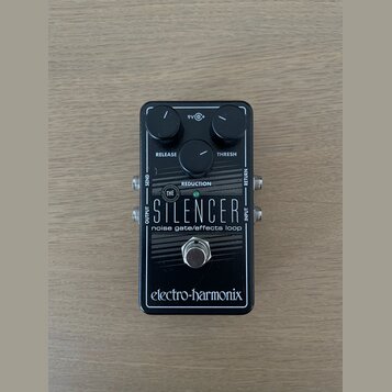 Černý efekt pedál s nápisy THE SILENCER a noise gate/effects loop. Na horní části jsou dva ovládací knoflíky s popisky RELEASE a THRESH, uprostřed je…