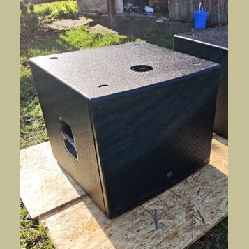 Černý subwoofer v kostkovém provedení s texturovaným povrchem. Přední strana je kryta kovovou ochrannou mřížkou, na které je umístěno malé logo JBL.…