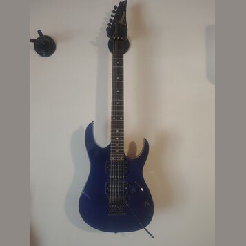 Modrá elektrická kytara s černým hmatníkem a černými hardwaremi. Na hlavě je nápis Ibanez. Kytara má dva humbuckery, jeden ovladač hlasitosti a jeden…