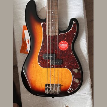 Elektrická basová kytara s korpusem v barevném přechodu od černé přes červenou k žluté. Nástroj má tmavě červený vzorovaný pickguard, na kterém je na…