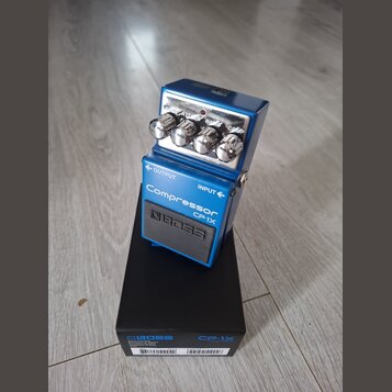 Modrý kompresorový pedál s nápisy Compressor CP-1X a logem BOSS. Na horní části jsou čtyři ovládací knoflíky s popisky SUSTAIN, ATTACK, RATIO a COMP.…