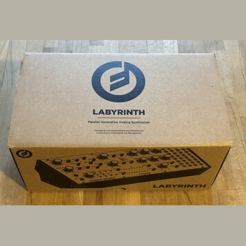 Hnědý kartonový krabic s nápisem LABYRINTH a textem Parallel Generative Analog Synthesizer. Pod tím je menší nápis Devoted to the Development and Man…