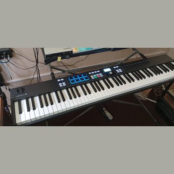 Černý MIDI kontrolér s klávesnicí, umístěný na stojanu. Na levé straně je nápis KEYLAB ESSENTIAL 61 a v horní části značka ARTURIA. Přístroj obsahuje…