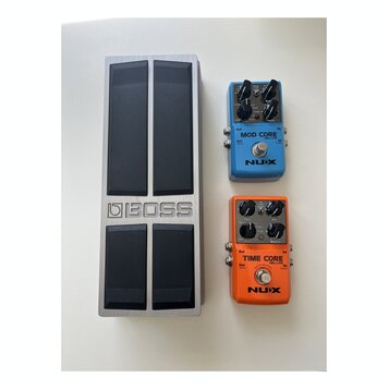 Na fotografii jsou tři efektové pedály. Vlevo je stříbrný kovový pedalboard s nápisem BOSS a čtyřmi velkými černými spínači. Vpravo nahoře je modrý p…