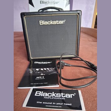 Černý kytarový kombozesilovač s texturovaným povrchem a zlatým lemem kolem mřížky. Na přední straně je bílý nápis Blackstar. Před zesilovačem leží už…