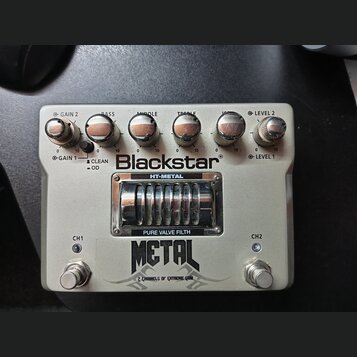 Bílá efektová pedál s nápisem Blackstar a modelem HT-METAL. Horní část obsahuje pět otočných potenciometrů s popisky GAIN 2, BASS, MIDDLE, TREBLE a L…